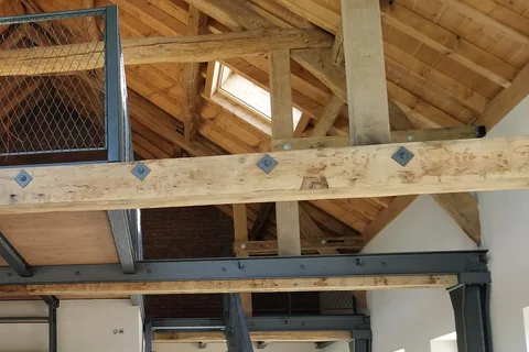 Umbau eines Gewerbebaus: alter Holzdachstuhl mit Dachfenster, darunter eine Stahlbühne mit Stahlträger, Stahlstütze und Treppe